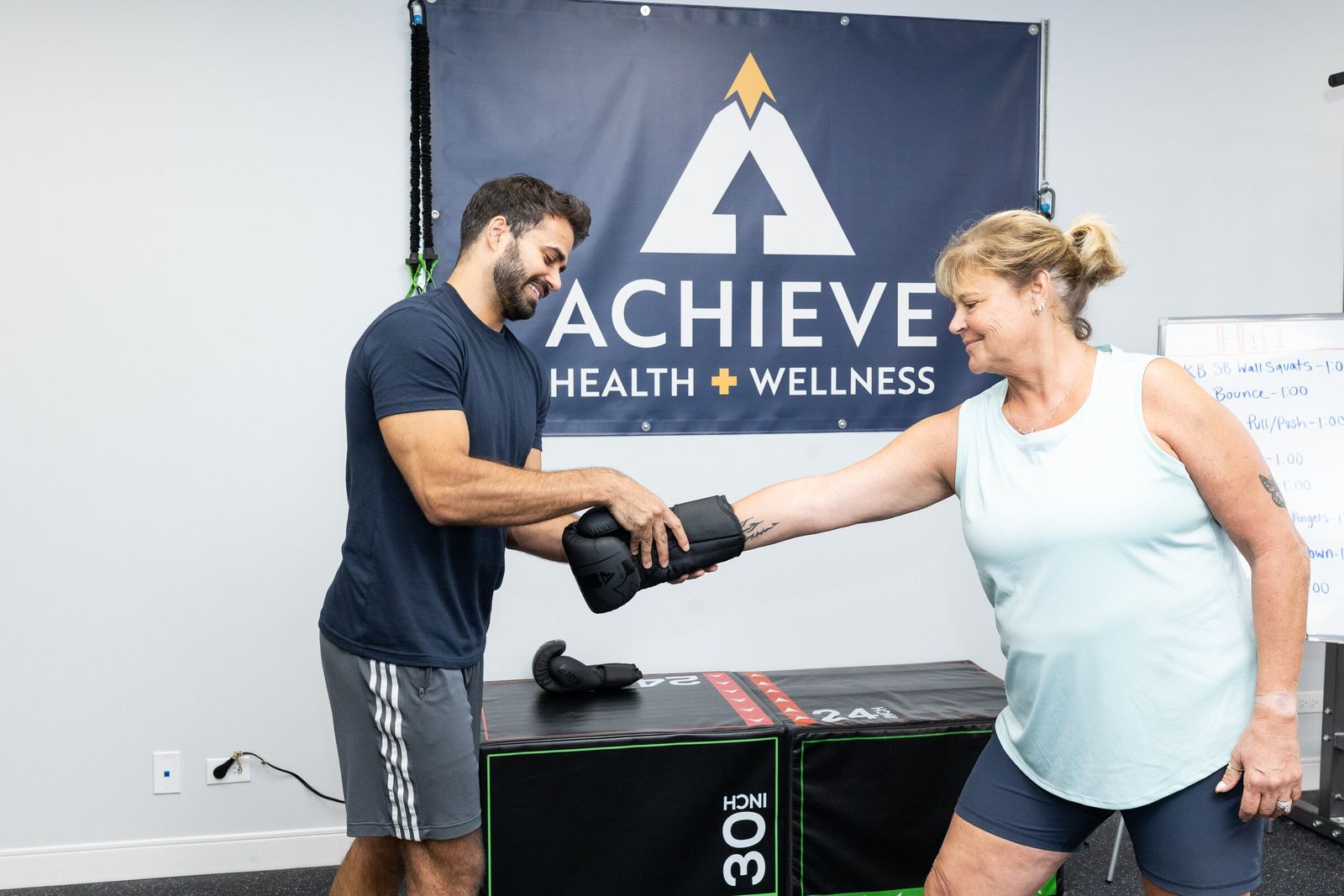 Trainer straps a boxing glove onto a client's wrist under the Achieve banner