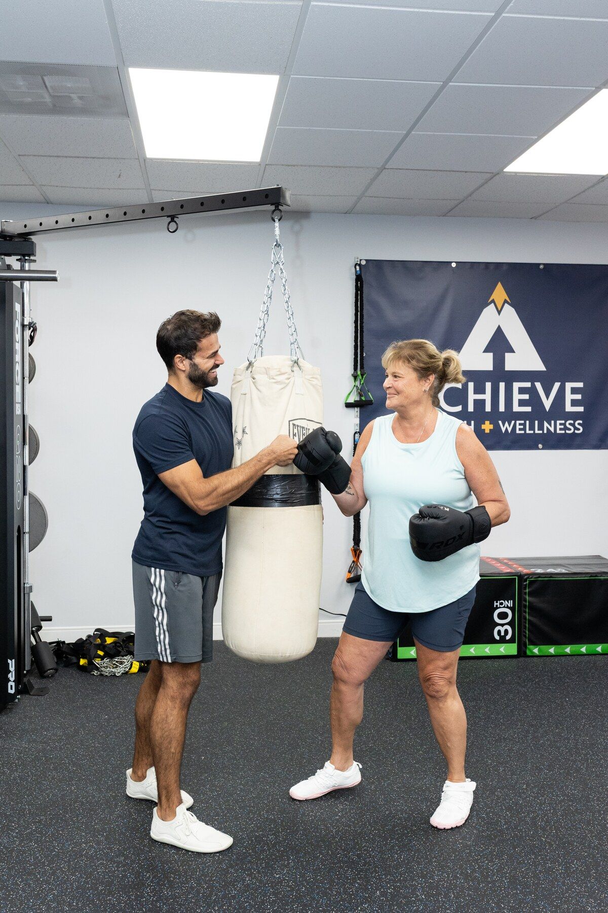 Trainer and client bump boxing gloves and smile beside the heavy bag