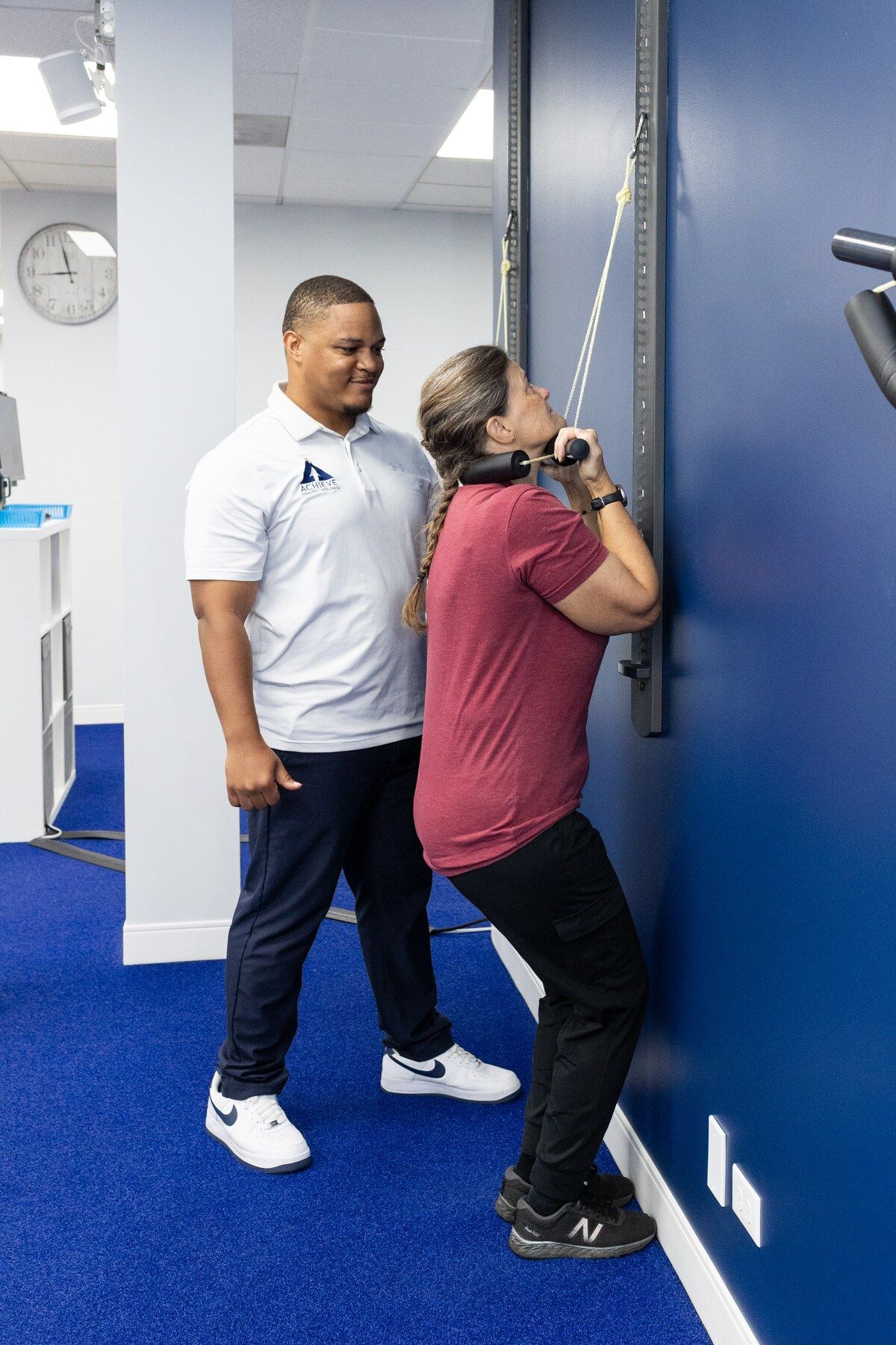 Smiling chiropractic assistant Charles Dennis watches a patient do a wall pulley neck exercise
