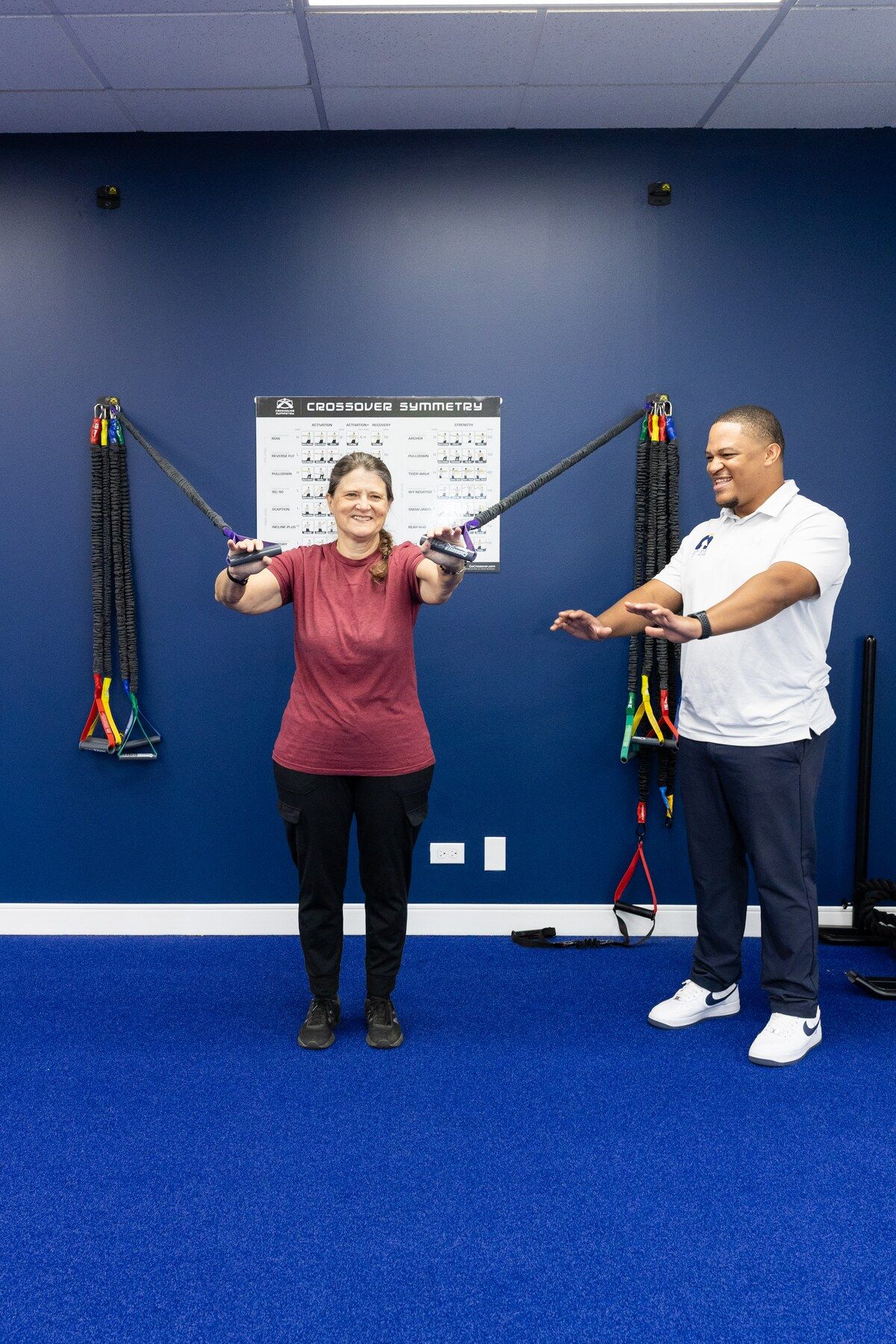 Patient smiles while pulling resistance bands on the shoulder chart as Charles Dennis coaches