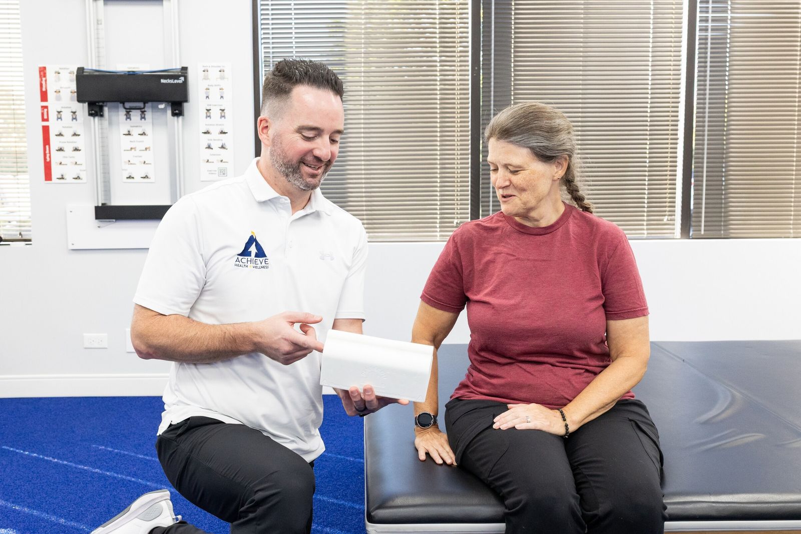 Smiling chiropractor shows a white cervical support block to a seated patient