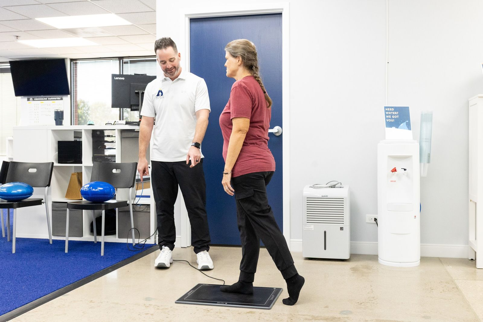 Chiropractor watches a patient step onto a foot pressure scanner plate in the clinic