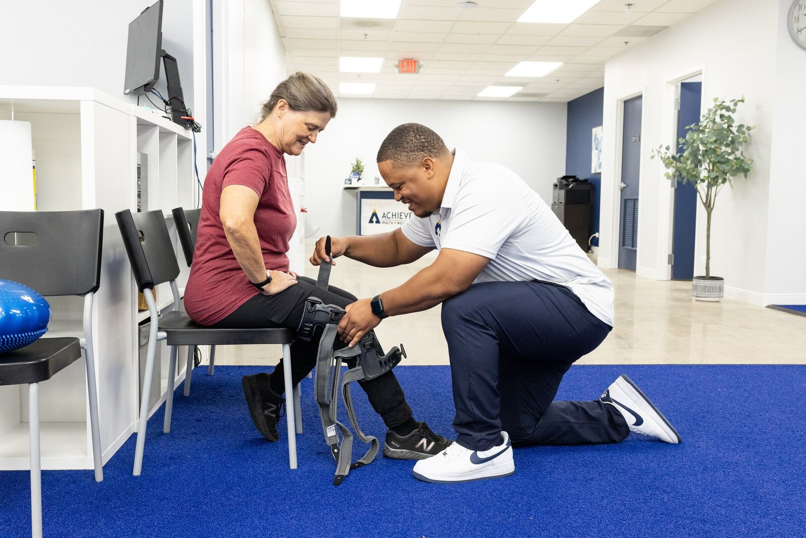 Charles Dennis tightens the strap of a hinged knee brace on a smiling seated patient