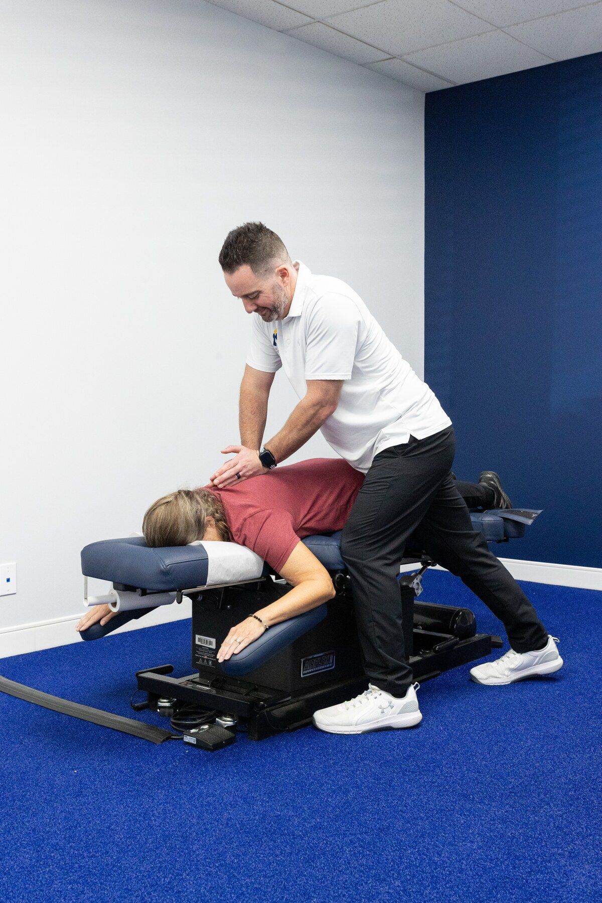 Smiling chiropractor adjusting the neck of a prone patient on a drop table