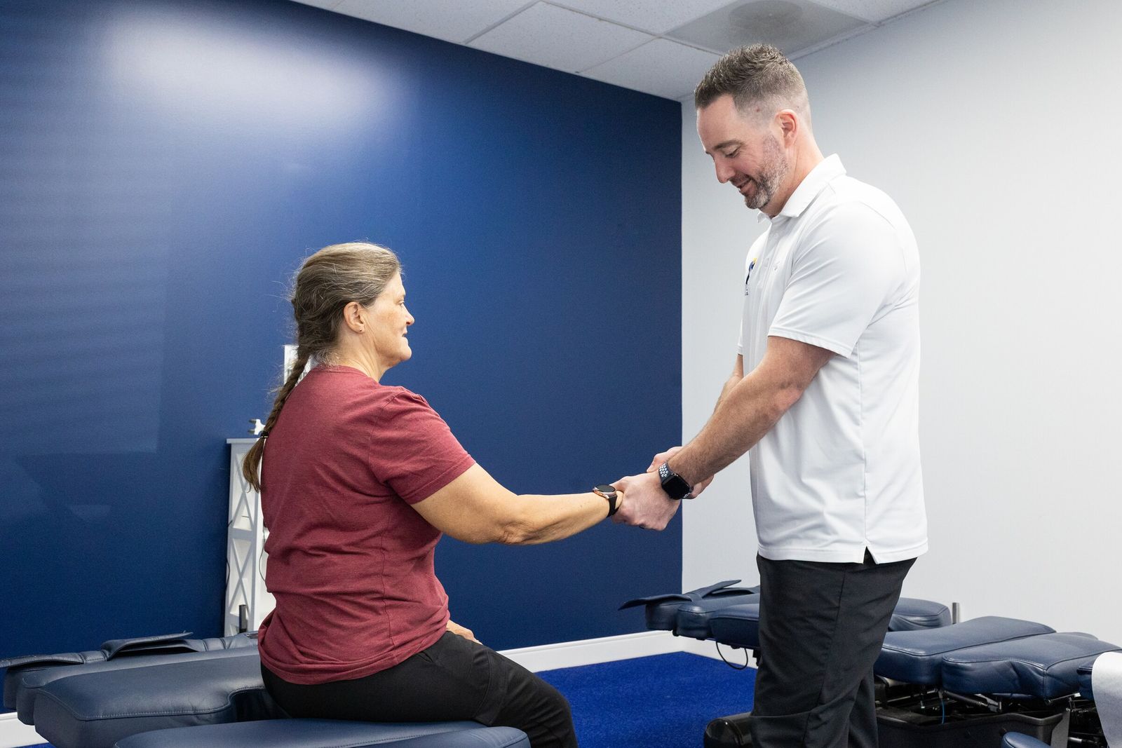 Chiropractor and smiling patient share a moment during a wrist assessment on a treatment table
