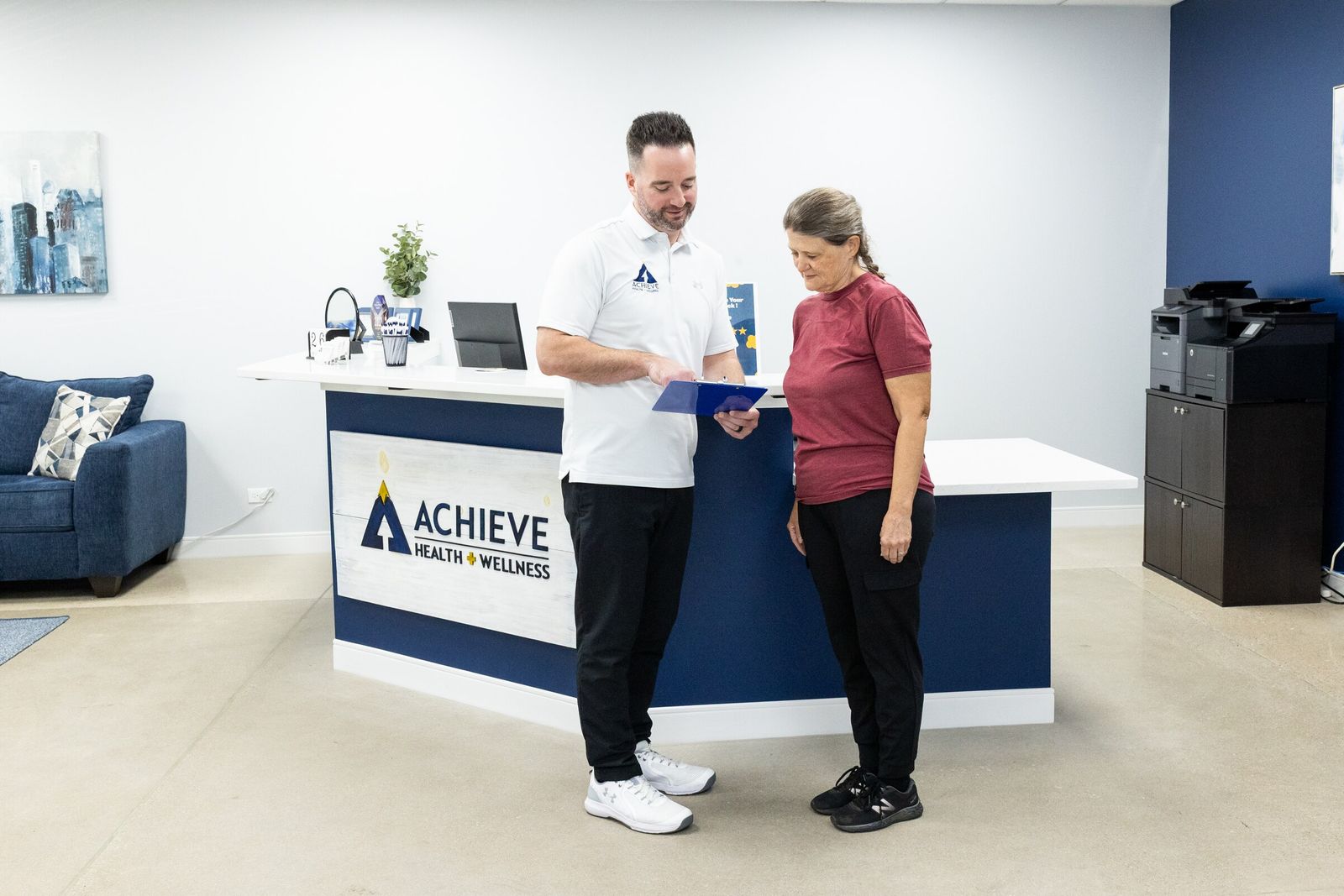 Chiropractor shows a patient a clipboard in front of the Achieve reception desk