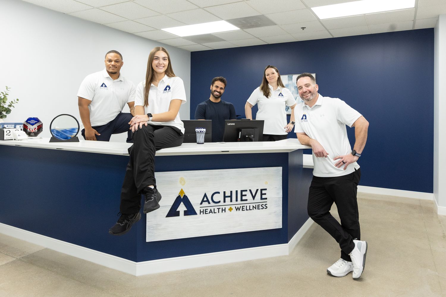 Achieve Health + Wellness team gathered around the reception desk in Bolingbrook